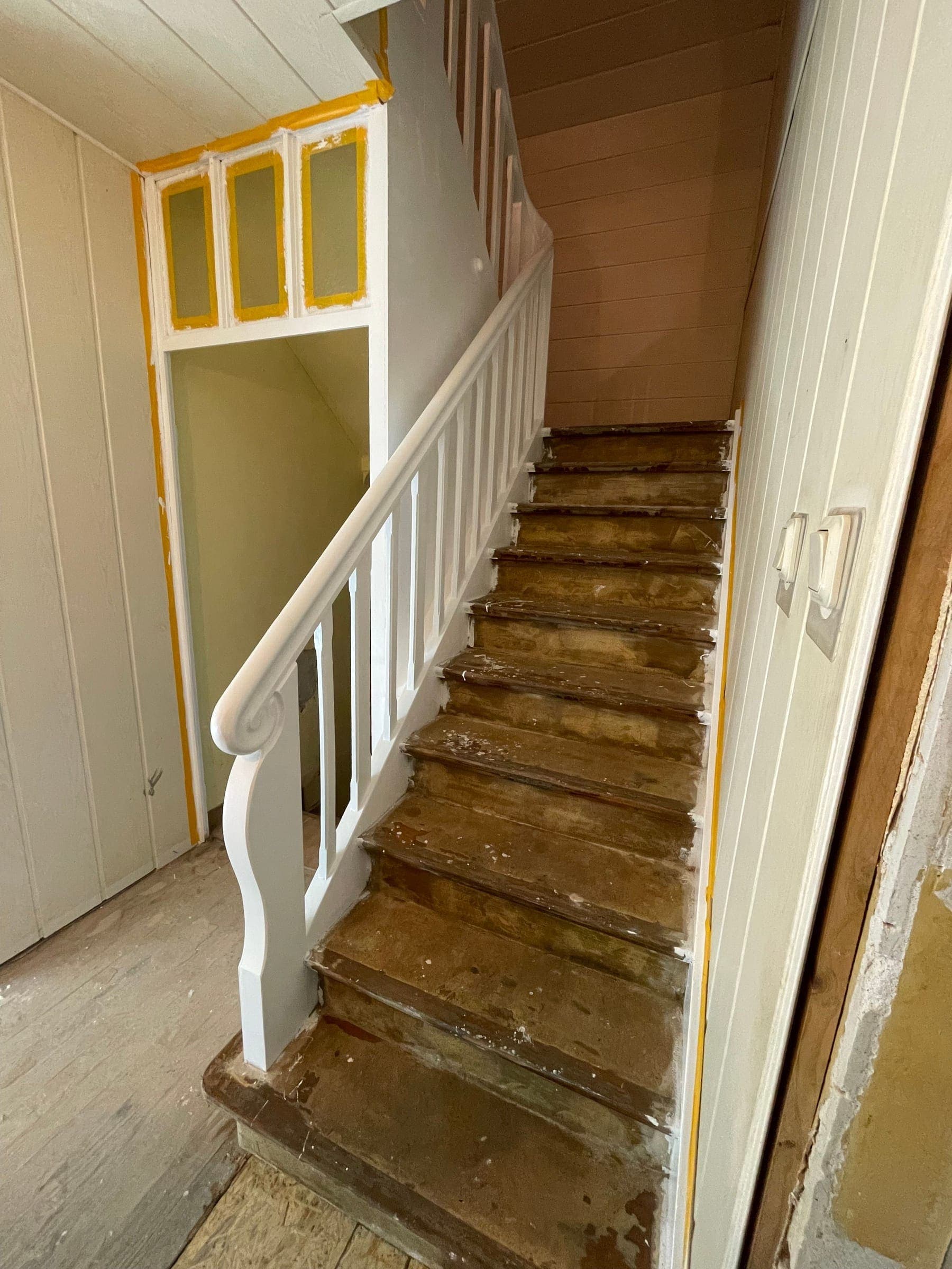 Treppe während der Renovierung: Stufen auf das rohe Holz abgeschliffen, Geländer und Wange frisch weiß lackiert, Klebeband an den Laibungen